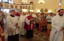 Księża idący przez środek kościoła. Wierni stoją w ławkach.