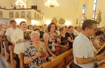 Wierni stojący w ławkach. Niektórzy trzymają wizerunek matki boskiej 